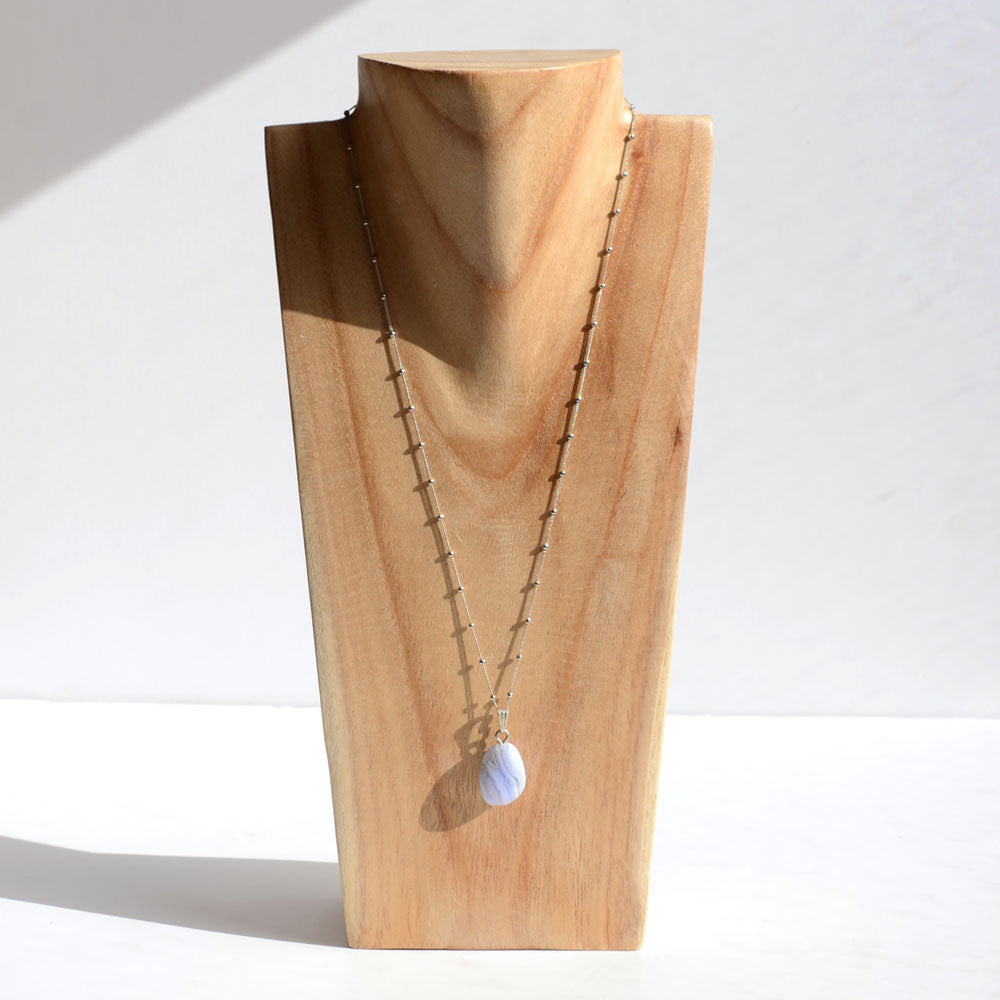 Photo d'un pendentif en pierre de Calcédoine bleue chaine en argent sur un portant en bois