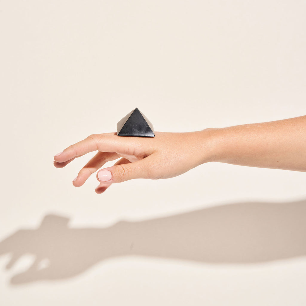 Photo d'une pierre de Shungite taillée en pyramide posée sur le dos d'une main